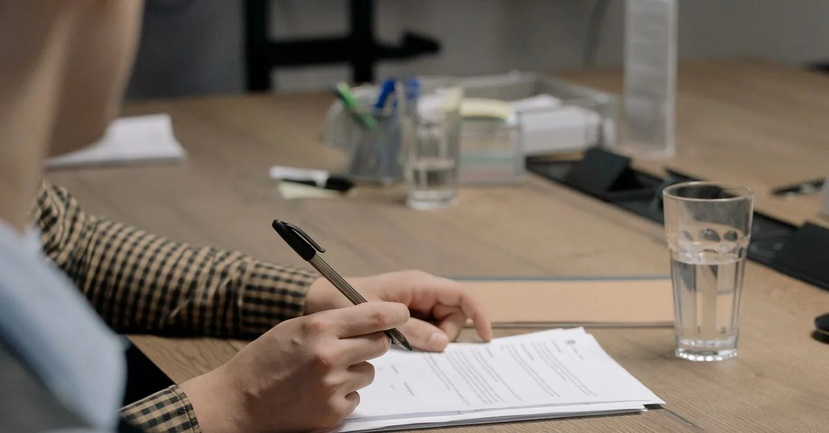 Person signing a document in an office at a wooden table